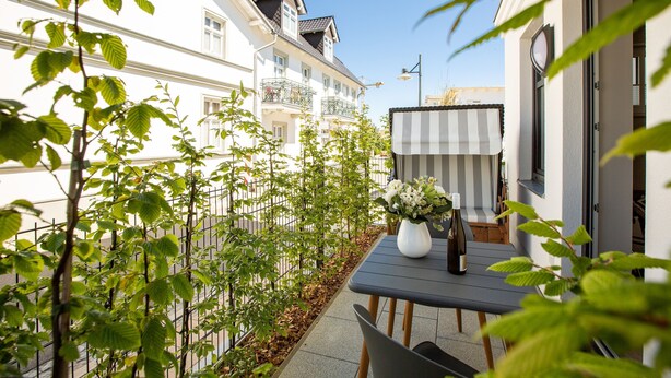 A balcony with a table, chairs, a vase with flowers, and a view of a white building with balconies. - Quartier Frohsinn, app. 04b (Heringsdorf)