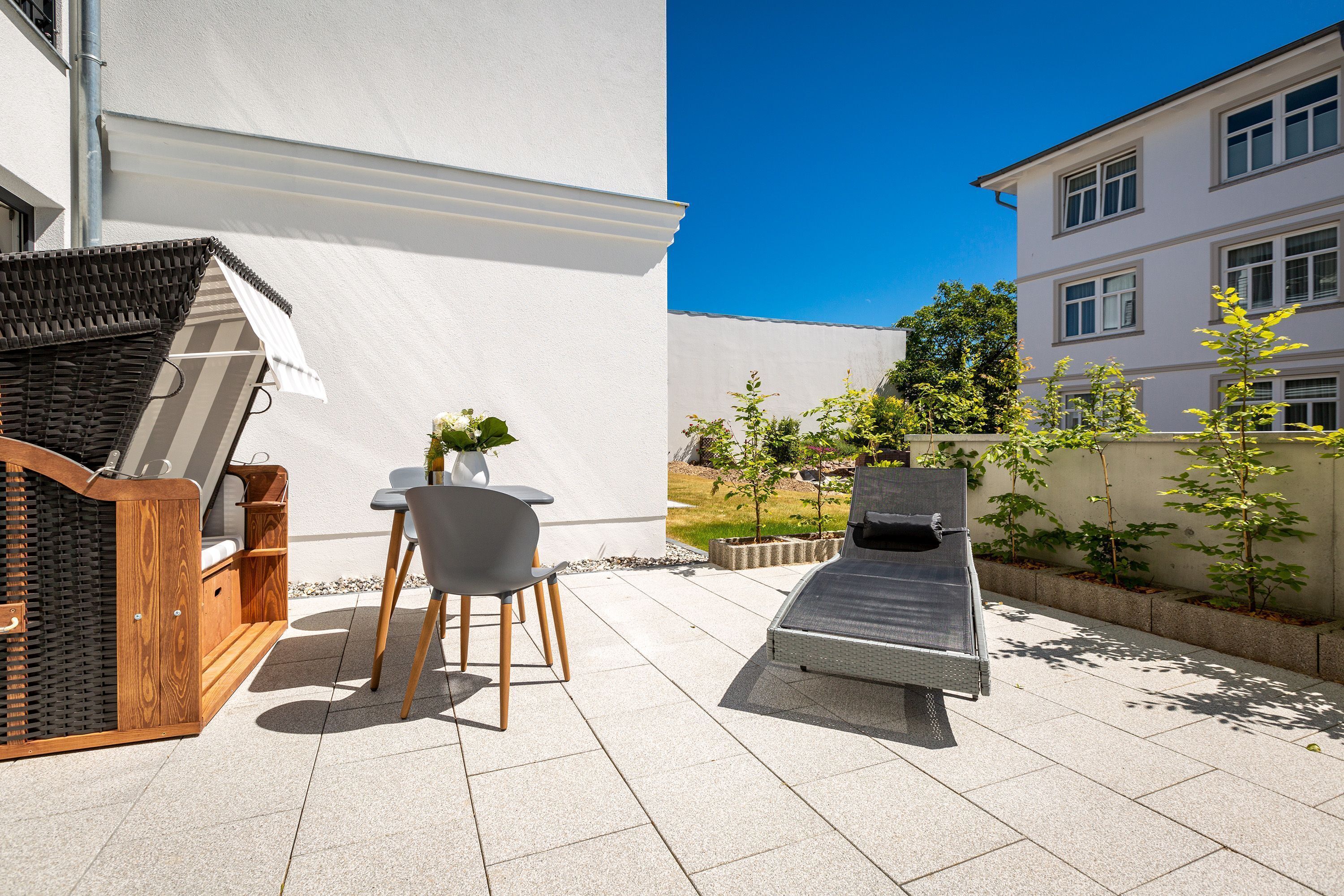 Eine Terrasse mit einer Holzbank, einem Tisch mit Stühlen und einem Grill.