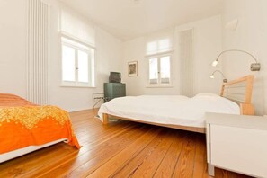 Ein Schlafzimmer mit zwei Betten, Holzboden, weißen Wänden und einer Heizung.