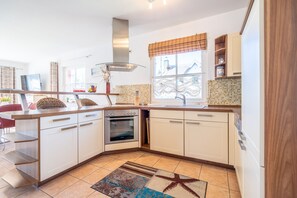 A modern kitchen with white cabinetry, a built-in oven, and a window with a view of a house. - Reethaus Koserow, Germany (Koserow)