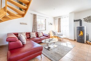 A modern living room with a red leather sofa, a glass coffee table, a fireplace, and a staircase.