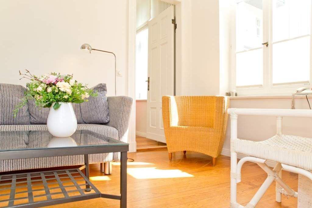 Un salon avec un canapé, un fauteuil en osier, une table blanche et un lampadaire.
