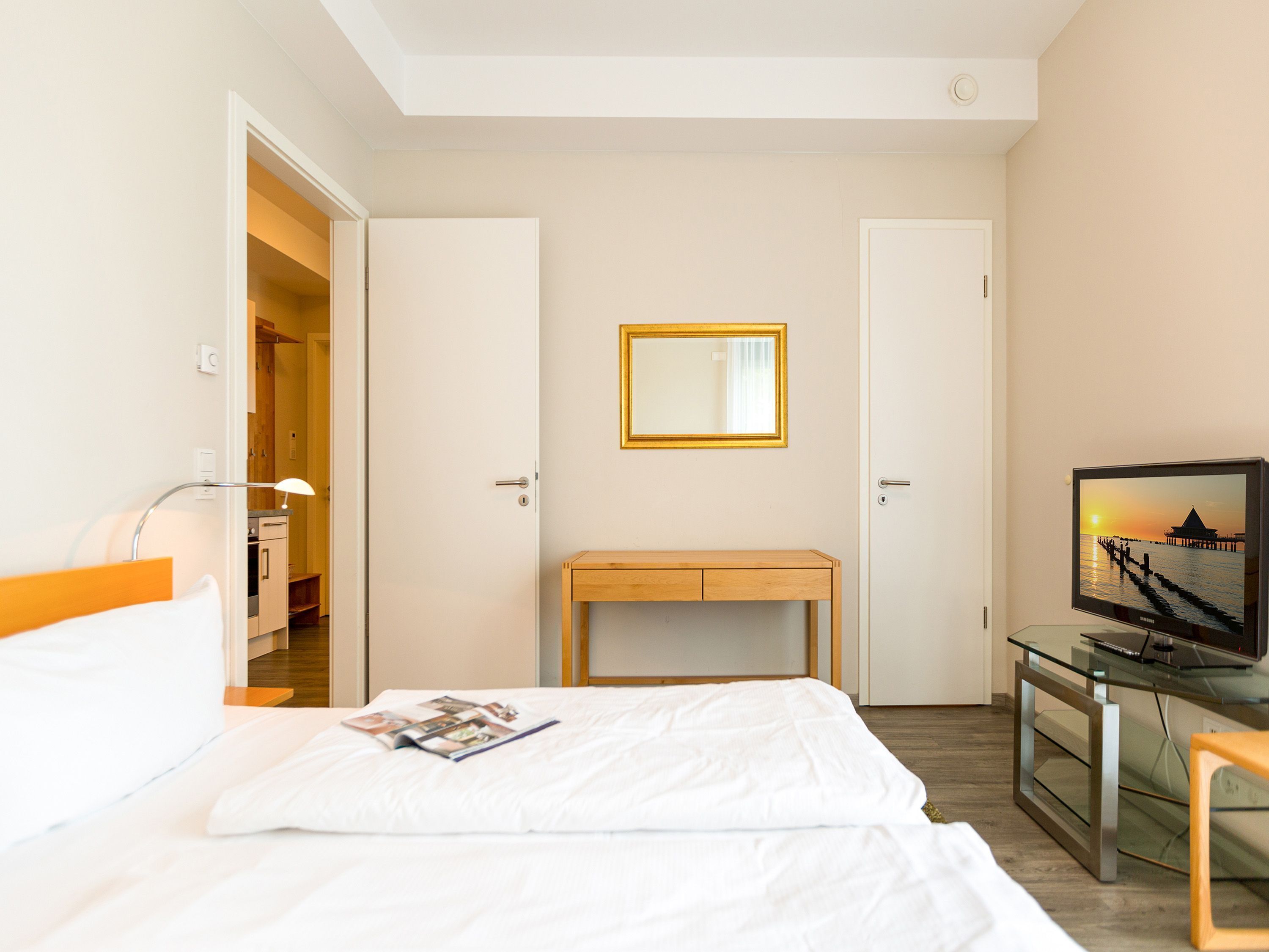 A hotel room with a bed, a bedside table, a TV, and a mirror on the wall.