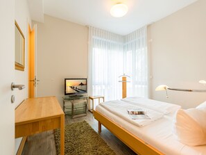 Una habitación de hotel con una cama, un escritorio, un televisor y una ventana con cortinas translúcidas.