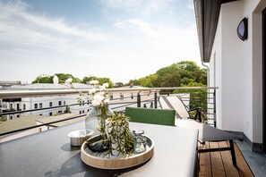 A balcony with a table set for two, a vase with flowers, and a view of buildings and trees. - Quartier Frohsinn, app. 12 (Heringsdorf)