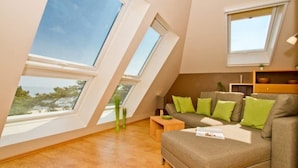 A modern living room with a sloped ceiling, large windows, a sofa with green cushions, and a wooden coffee table. - Villa Strandperle, App. 32a (Heringsdorf)