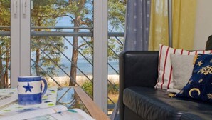 Quarto com vista para o mar, um sofá de couro com almofadas estampadas e uma mesa com uma caneca e papéis.