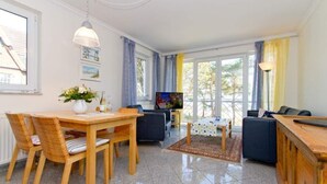 Uma sala de estar moderna com área de jantar, televisão e uma janela grande com cortinas.