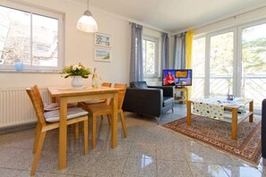 Un salon bien éclairé, comprenant un coin repas, un téléviseur et offrant une vue sur l’extérieur.