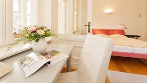Una habitación de hotel con una cama, una mesita de noche con una revista, un jarrón con flores y una ventana con vista a la ciudad.