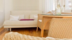 Ein gemütliches Wohnzimmer mit einer Couch, einem Korbstuhl und einem Glastisch mit Flaschen.