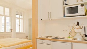 Ein kleines Zimmer mit einem Bett, einer kleinen Küchenzeile inklusive Mikrowelle und Spüle.