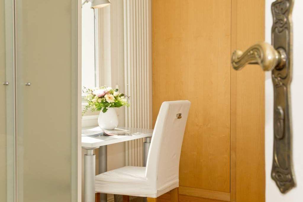 Una habitación con una puerta de madera, una silla blanca y una mesa pequeña con un jarrón de flores.