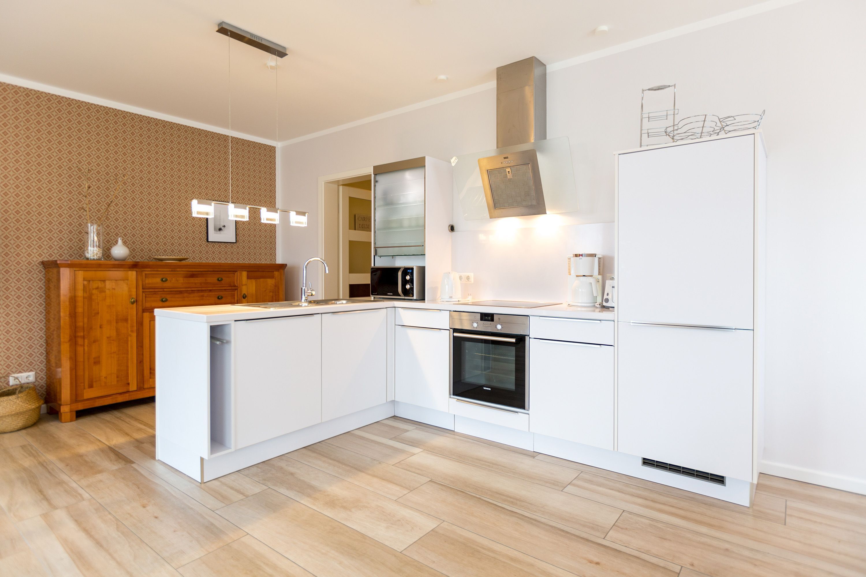 Eine moderne Küche mit weißen Schränken, einem eingebauten Ofen, einer Edelstahl-Dunstabzugshaube und einem weißen Kühlschrank.