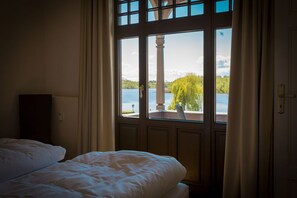 A bedroom with a large window overlooking a lake and greenery. - Villa Strandklause, App. 3 (Heringsdorf)