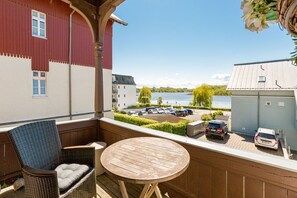 Ein Balkon mit Korbstuhl und rundem Tisch, mit Blick auf einen Parkplatz und ein Gewässer.