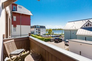 A balcony with a wooden chair, a view of a parking area, and buildings in the background. - Villa Strandklause, App. 3 (Heringsdorf)