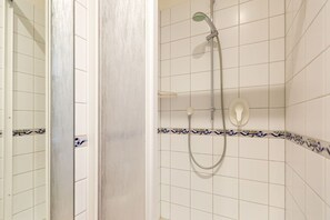 Uma casa de banho com azulejos brancos, chuveiro com barra de mão e sanita.