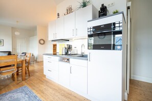 A modern kitchen with white cabinets, stainless steel appliances, and a wooden dining table. - Villa Strandklause, App. 3 (Heringsdorf)
