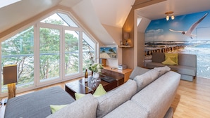 A modern living room with a large window, a sofa, a coffee table, and a mural of a seascape.