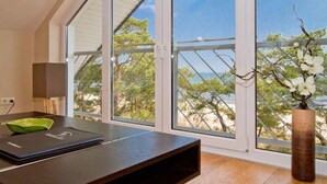 A modern room with a large window overlooking a beach, a wooden table, and a vase with flowers.