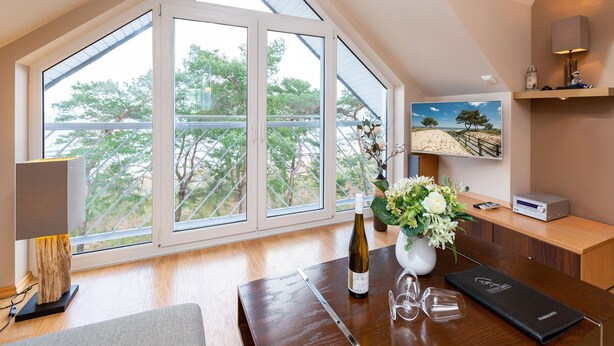 A room with a large skylight, a wooden desk, a wine bottle, and a vase of flowers.