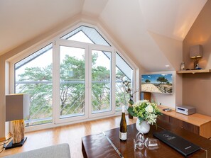 A room with a large skylight, a wooden desk, a wine bottle, and a vase of flowers. - Villa Strandperle, App. 32 (Heringsdorf)