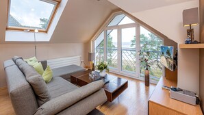 A modern loft bedroom with a sloped ceiling, skylights, a large window, a sofa, a coffee table, and a side table with a lamp.