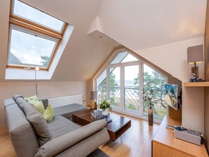 A modern loft bedroom with a sloped ceiling, skylights, a large window, a sofa, a coffee table, and a side table with a lamp. - Villa Strandperle, App. 32 (Heringsdorf)