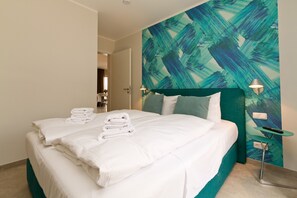 A neatly made bed with white linens and towels, a teal accent wall, and a small bedside table with a lamp. - Quartier Ahlbeck, app. 01 (Heringsdorf)