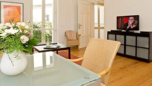 Un salon avec une table à plateau en verre, un fauteuil en osier et un téléviseur posé sur un meuble noir.