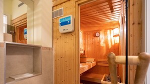 Sauna, jossa on puuseinät, -penkit ja ohjauspaneeli, jossa lukee ”SAUNA”.