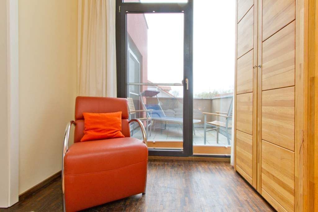Una habitación con una butaca de cuero rojo, un armario de madera y una puerta de cristal que da a un espacio exterior con una mesa y sillas.