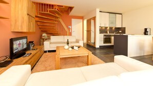 A modern living room with a sofa, a coffee table, and a TV. There is a staircase leading to another level. - Quartier 47, App. 05 (Heringsdorf)