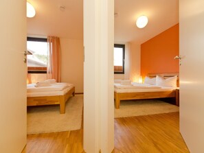 Una habitación con dos camas de madera, alfombra blanca y una ventana con cortinas.