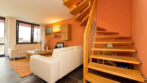 A modern living room with a white sofa, a wooden staircase, and a TV on a wooden stand. - Quartier 47, App. 05 (Heringsdorf)