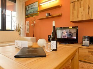 Sala de estar com mesa de centro de madeira, uma garrafa de vinho, controle remoto e um laptop.