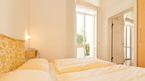 A bedroom with two beds, a bedside table with a lamp, and a door leading to another room. - Villa Artemis, 01 Piraeus (Heringsdorf)