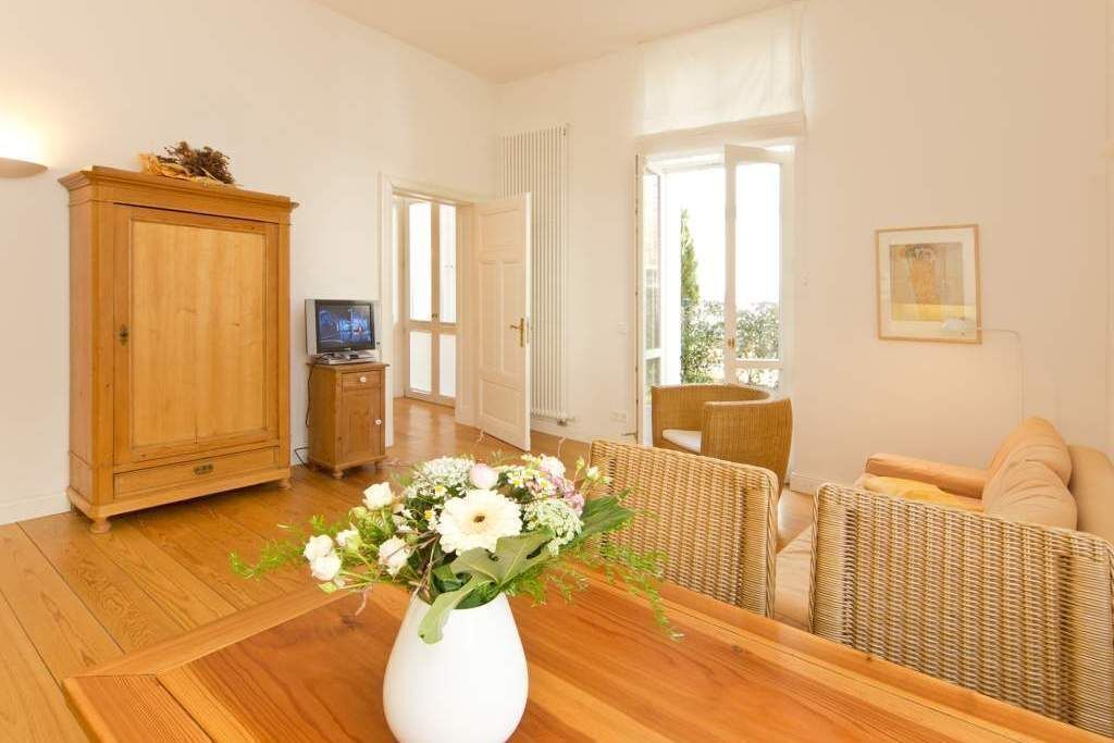 Une pièce comprenant une table à manger en bois, un vase blanc orné de fleurs, des meubles en osier, un téléviseur et une porte donnant sur l’extérieur.