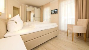 Hotellihuone, jossa on suuri sänky, tuoli, yöpöytä, peili ja taulu seinällä.