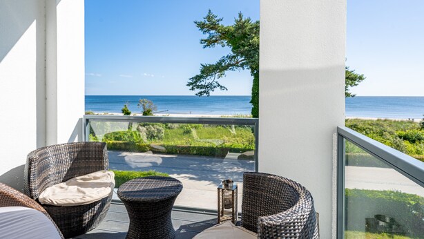 Un balcone con mobili in vimini, ringhiera in vetro e vista sul mare.