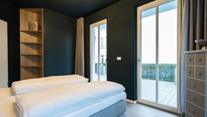 A bedroom with a bed, a wardrobe, a shelf unit, and a sliding glass door to a balcony.