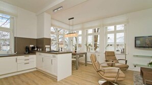 A modern kitchen with white cabinets, a central island, and a dining area with a table and chairs. - Villa Waldschloss, app. 06 (Heringsdorf)