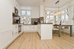 Een moderne keuken met witte kasten, een centraal eiland en een eetgedeelte met een tafel en stoelen.