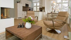 A modern living room with a fireplace, a dining area, and a kitchen in the background. - Villa Waldschloss, app. 06 (Heringsdorf)