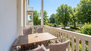 A balcony with a table and wicker chairs, overlooking a residential area with trees and houses. - Villa Waldschloss, app. 04 (Heringsdorf)