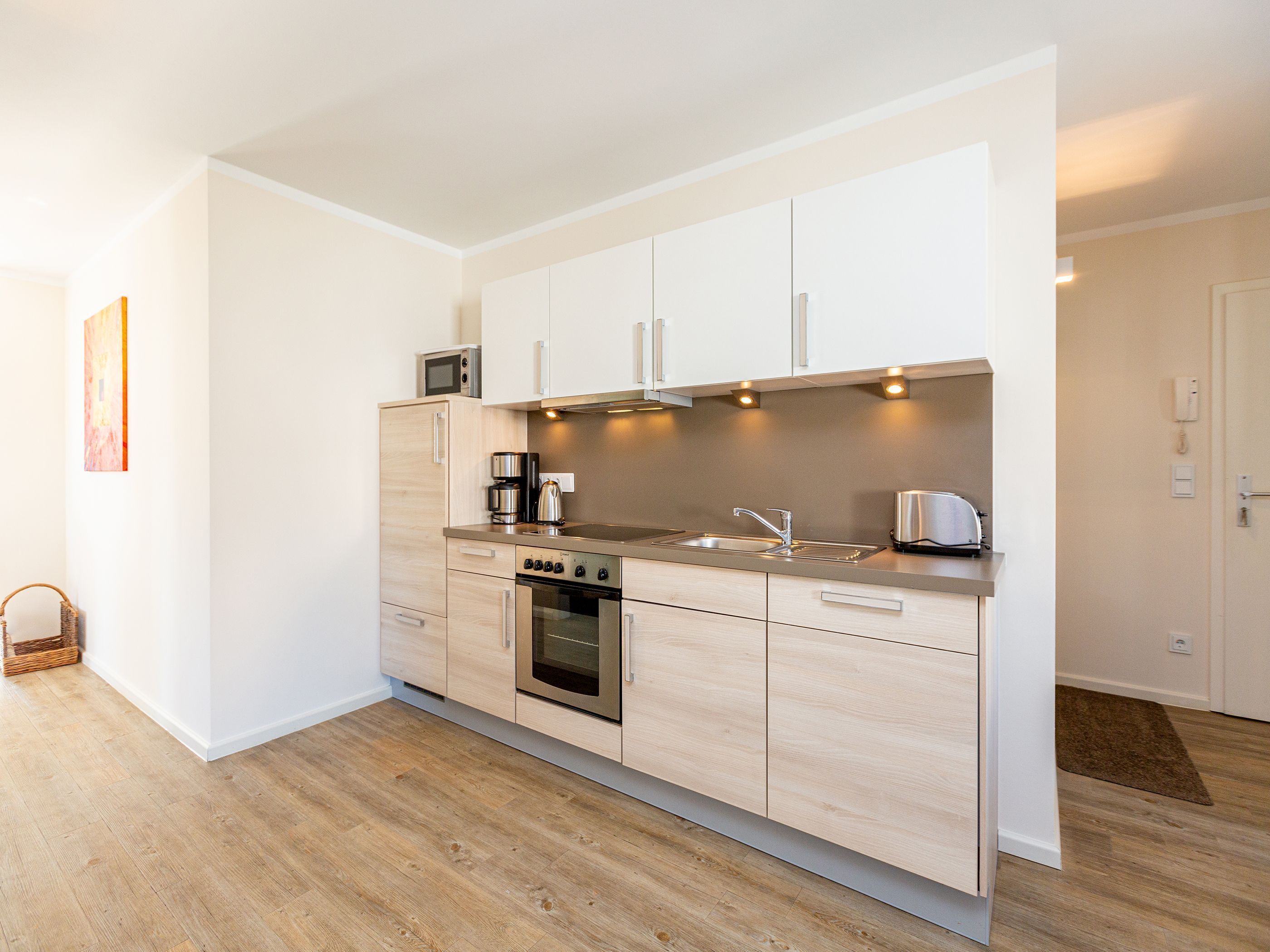 A modern kitchen with light wood cabinets, stainless steel appliances, and a built-in oven.