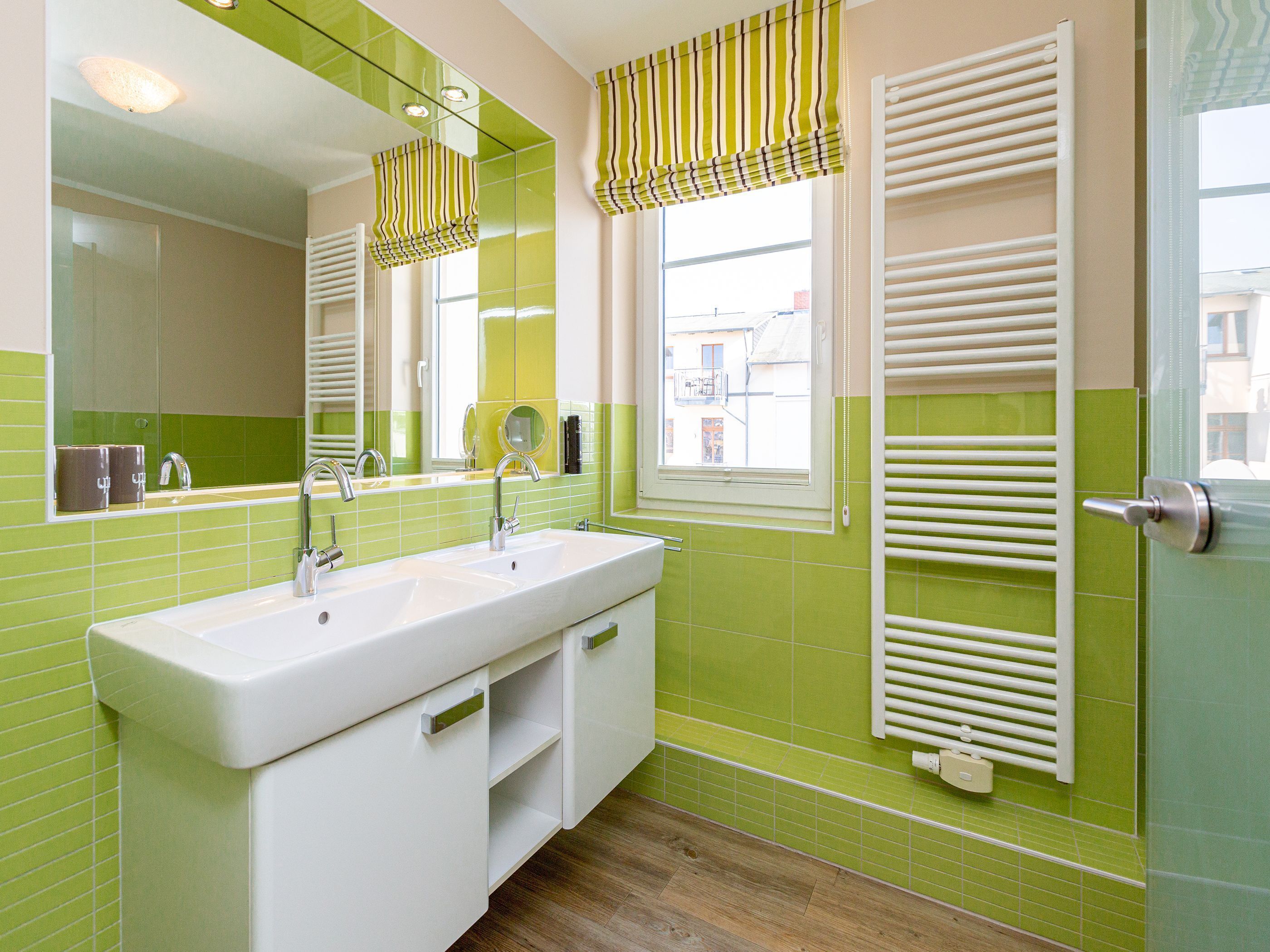 A bathroom with a white sink, green tiles, a mirror, and a window with blinds.