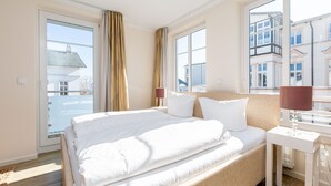 Una camera d'albergo con un letto grande, un comodino con una lampada, una finestra con tende e vista sugli edifici esterni.