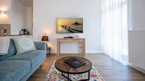 A modern living room with a sofa, coffee table, and a painting of a sunset over water. - Villa Waldschloss, app. 01 (Heringsdorf)